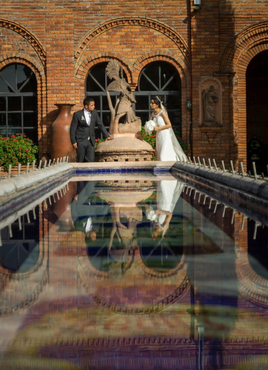 A bride and groom stand romantically by a reflecting pool at a historic venue, capturing timeless elegance.