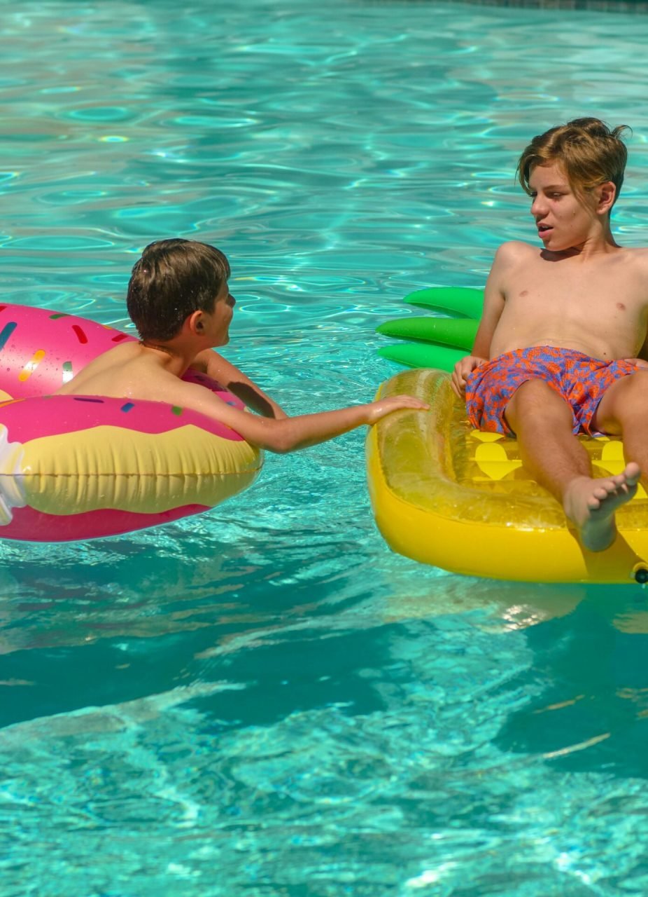 Two boys having fun in a pool with colorful inflatable floaties on a sunny day.